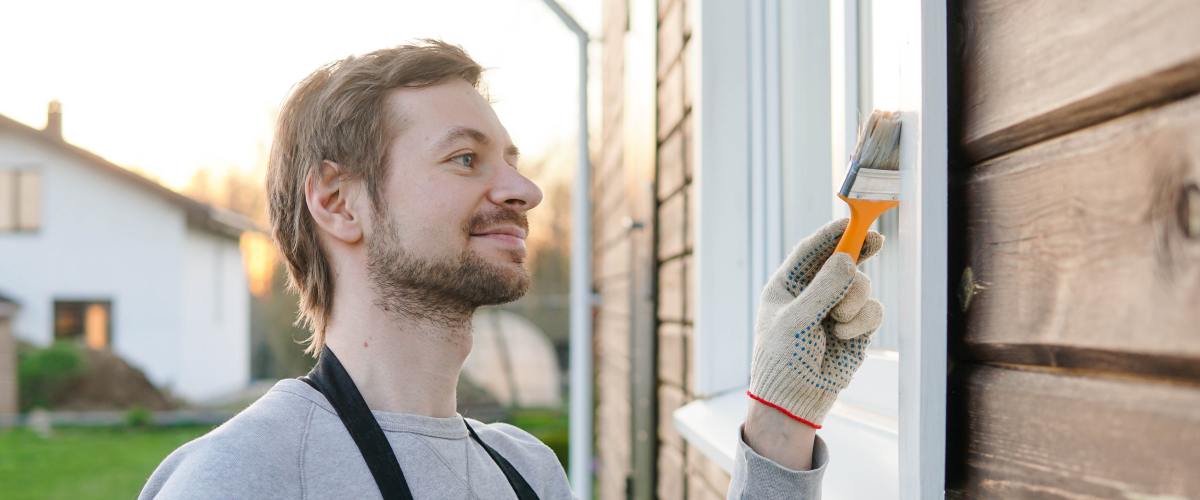 Man outside painting a windowsill white.